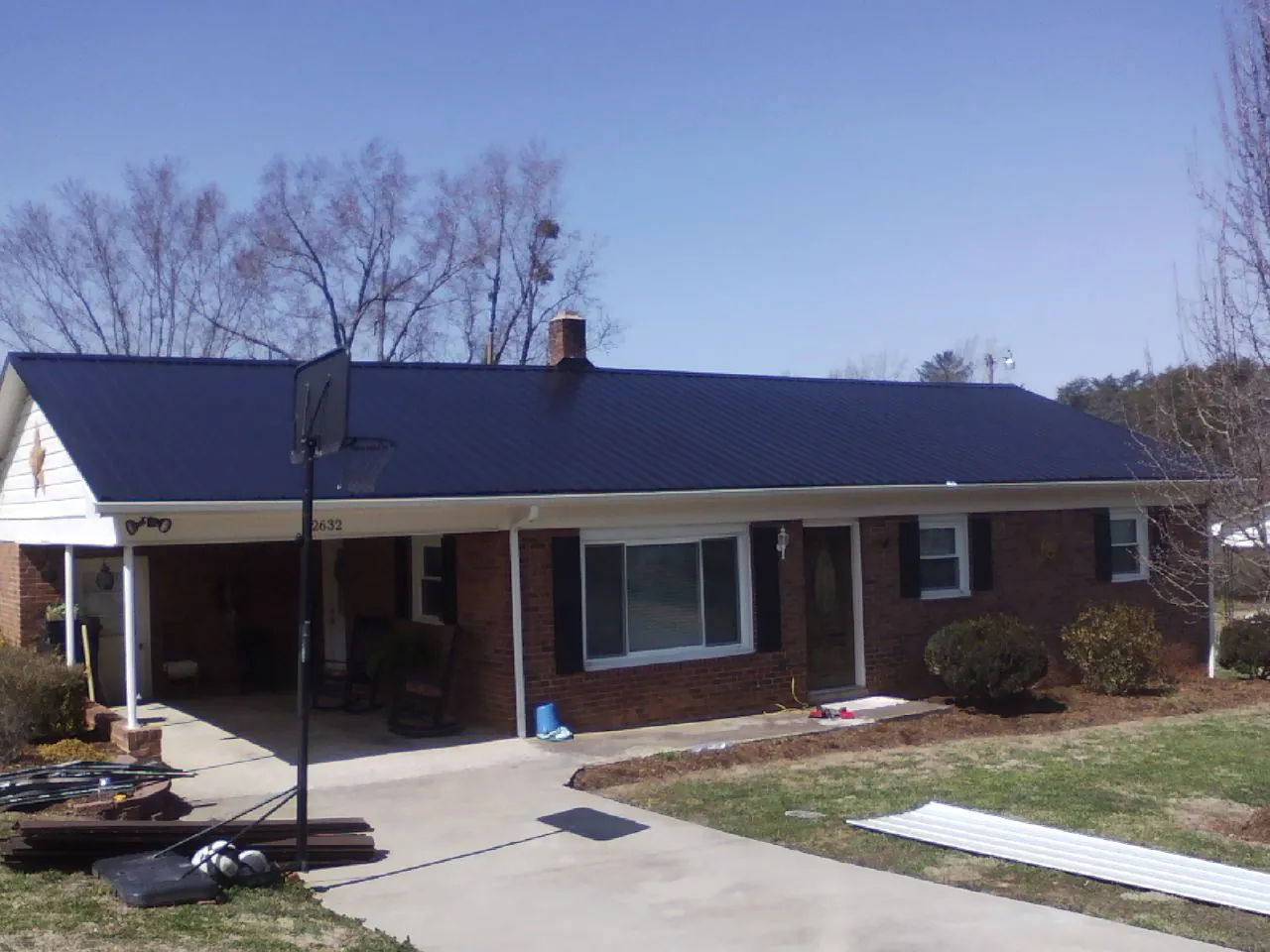 Finished dark blue metal roof on a brick ranch with a carport in Rice