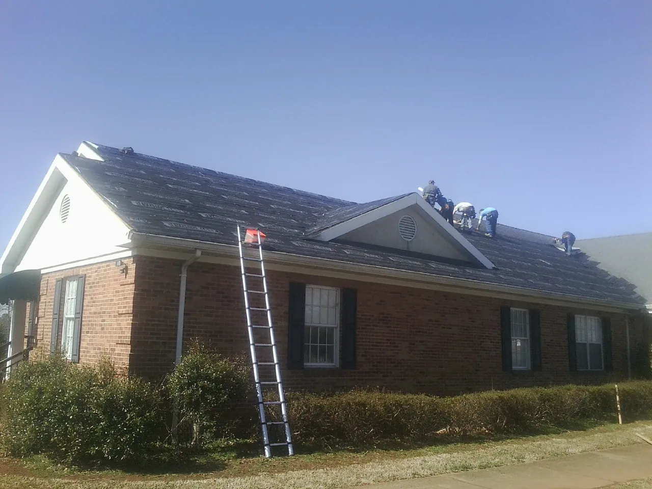 Crew tearing shingles off a brick ranch roof with a ladder set — Emergency Roof Repair work by our crew in Rice