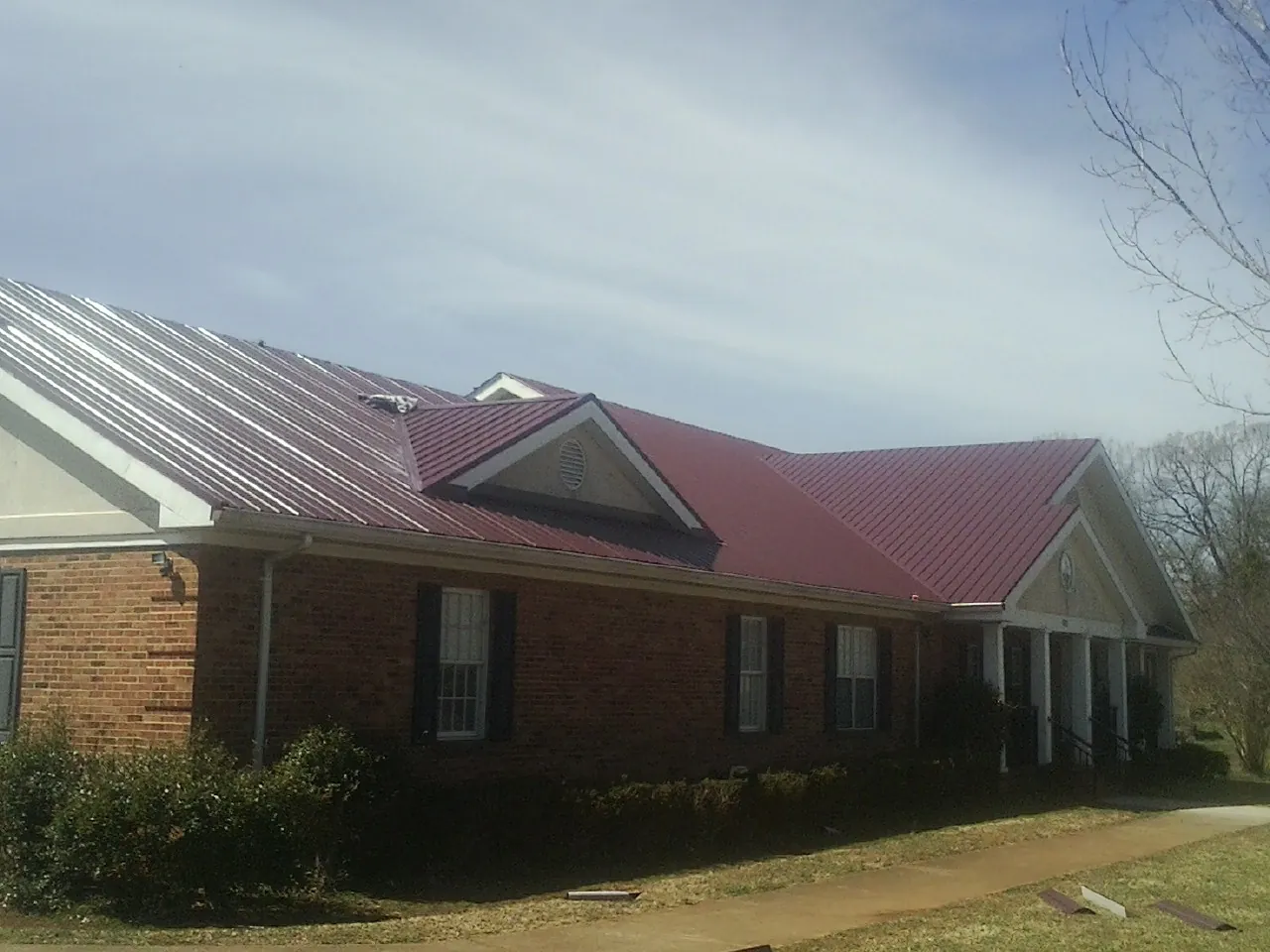 Red metal roof with gabled entries on a long brick building, from a Hail Damage Roof Repair job in Rice