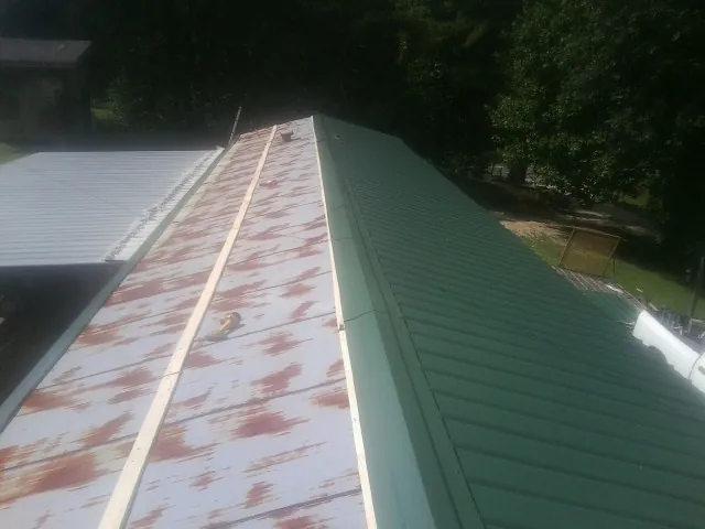Old rusted panels beside newly installed green metal roofing — Wind Damage Roof Repair by Roofing Brothers in Rice